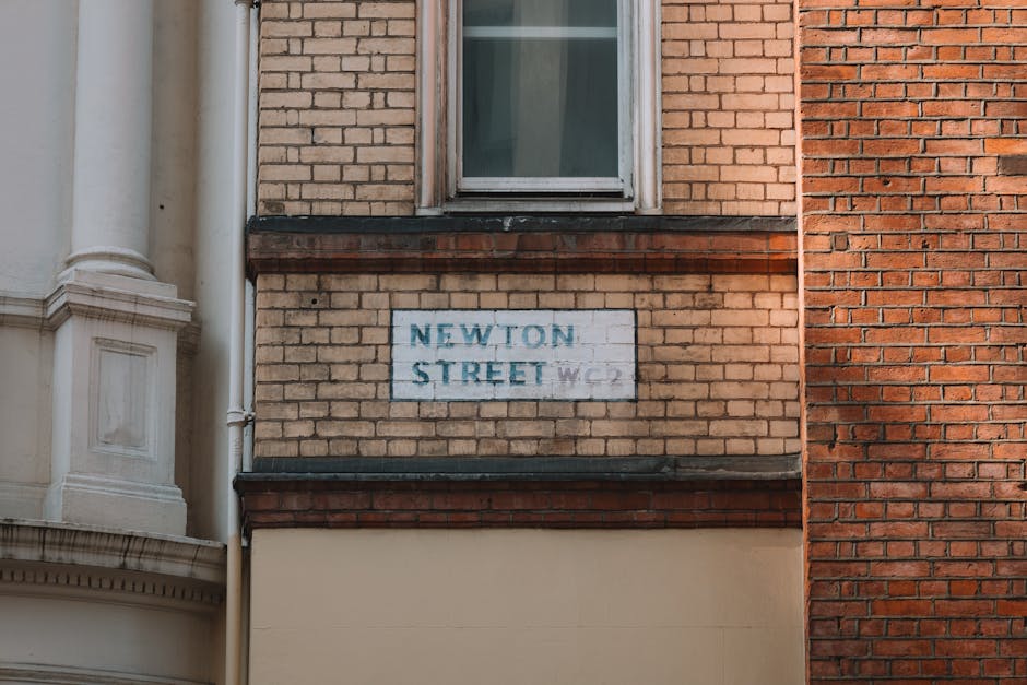 A close-up view of a brick building on Newton Street, featuring a weathered street sign with faded blue lettering mounted on the brick wall. The sign reads 'NEWTON STREET W.C. 2' and is surrounded by 